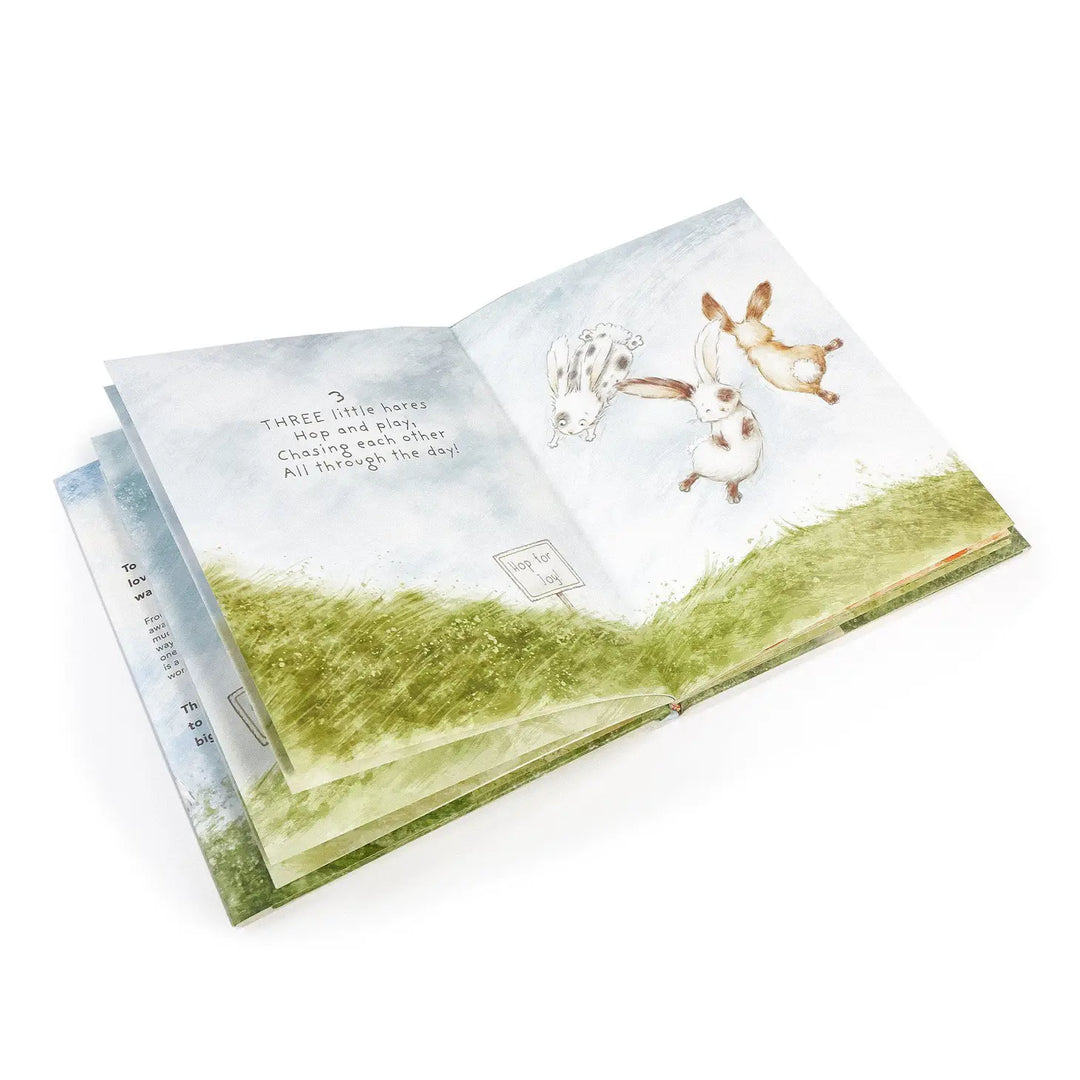 Open children's book showing three illustrated bunnies hopping across green meadow with blue sky