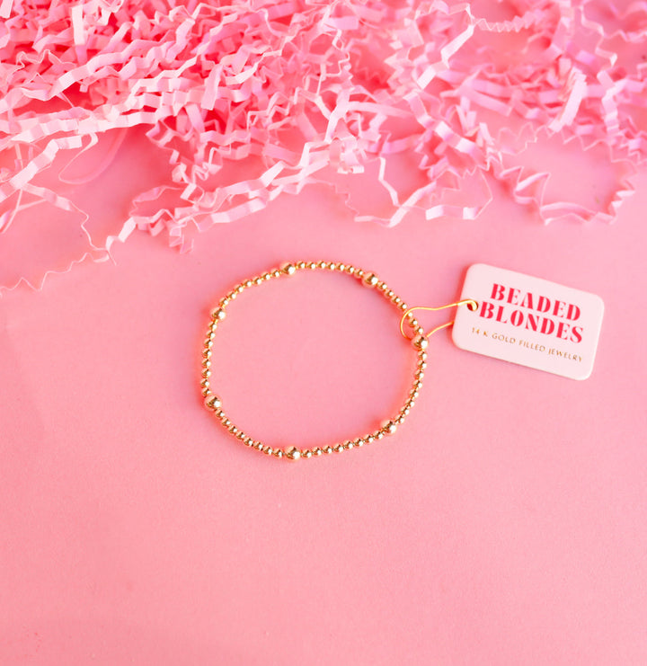Beaded Blondes Olive Bracelet in 14K gold-filled beads on pink background with tag.