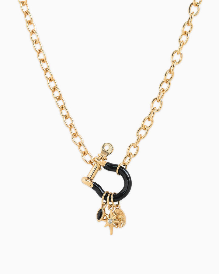 Gold chain necklace with black enamel horsebit carabiner and three hanging charms including star and crystal