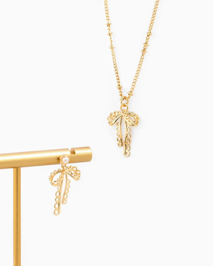 Gold lace bow ball station necklace with delicate chain and matching bow earring displayed on stand