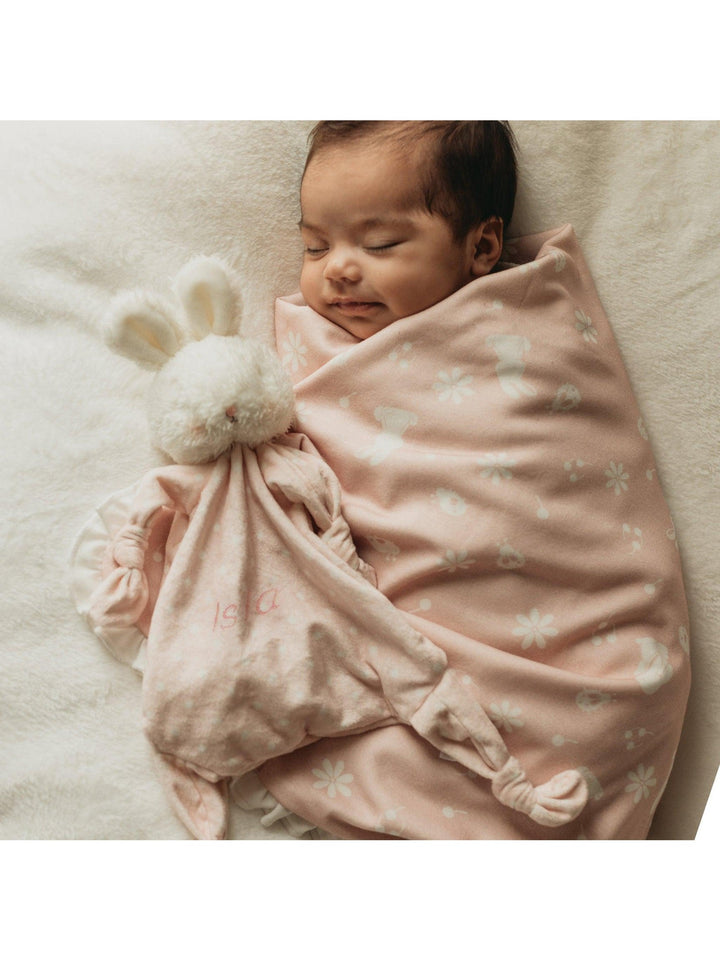 Baby swaddled in pink floral blanket holding white bunny lovey toy