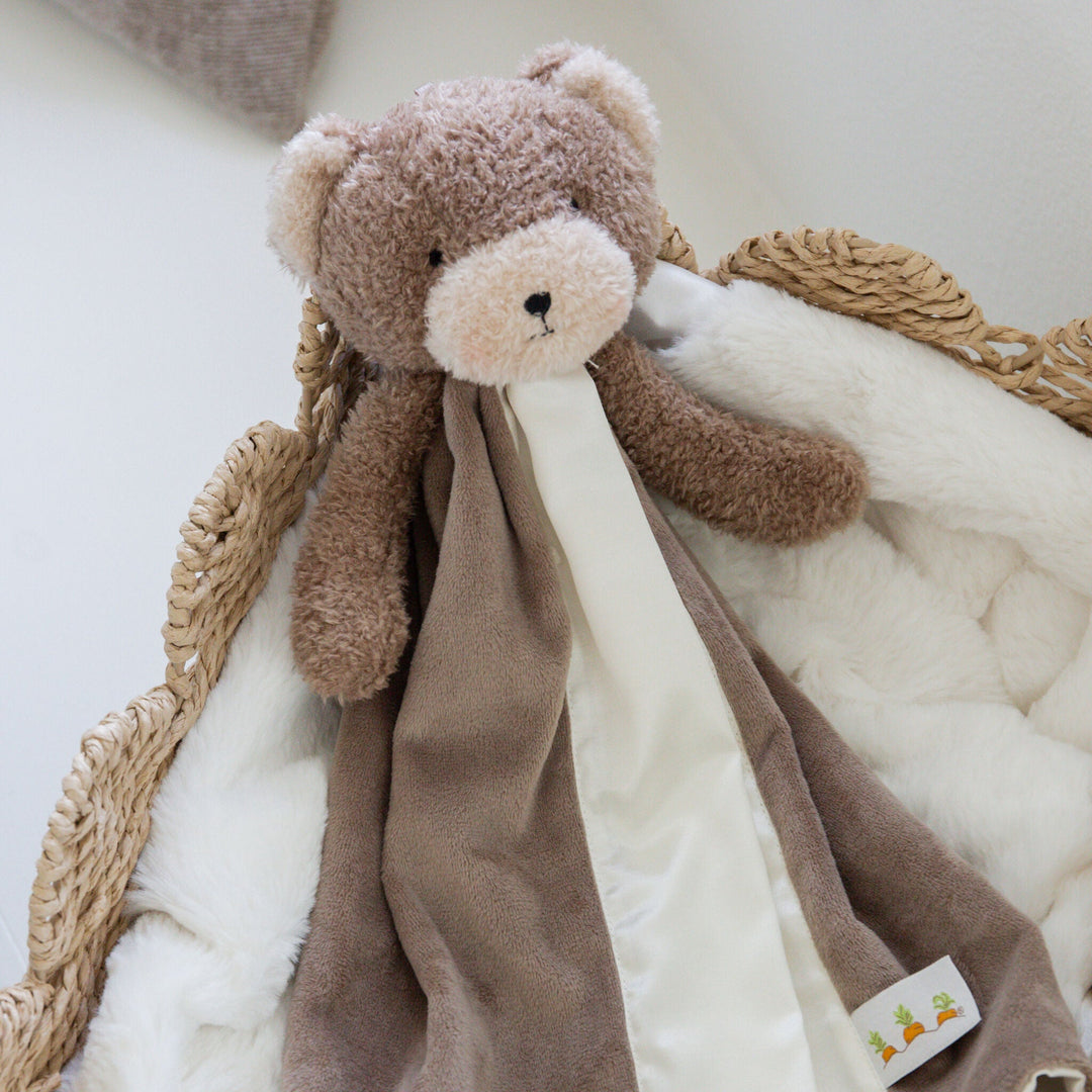 Brown teddy bear security blanket with soft cream fabric strips in wicker basket