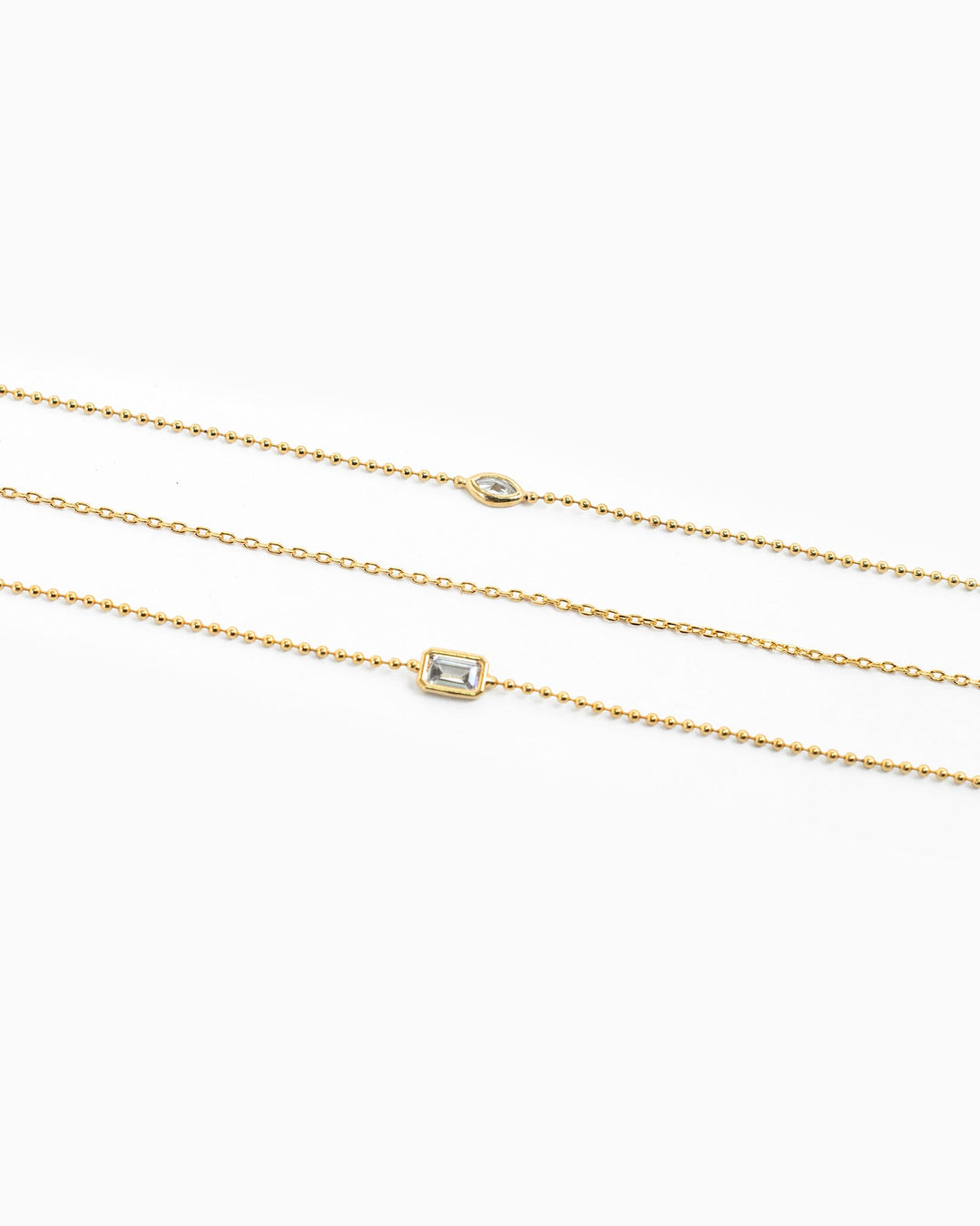 Three layered gold necklaces featuring bezel-set marquise and baguette CZ pendants on delicate chains