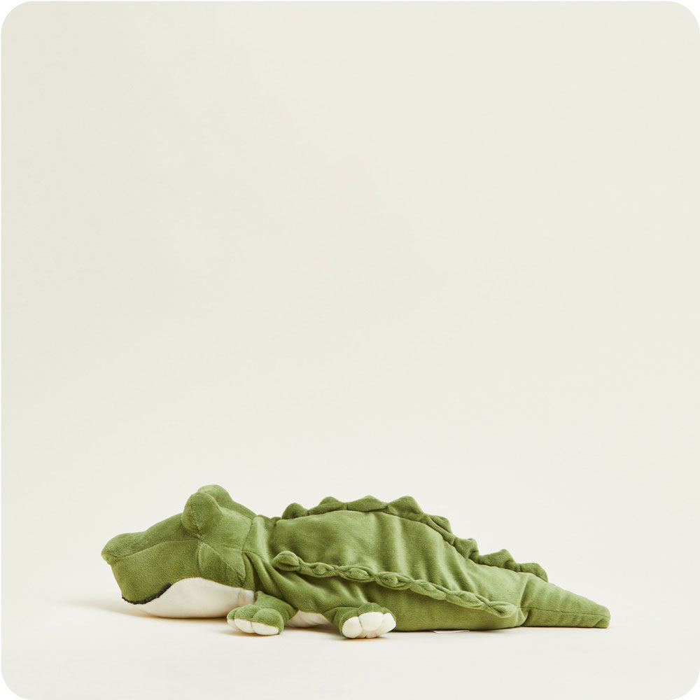 Green alligator Warmies plush heating pad with spikes and tail lying on white background