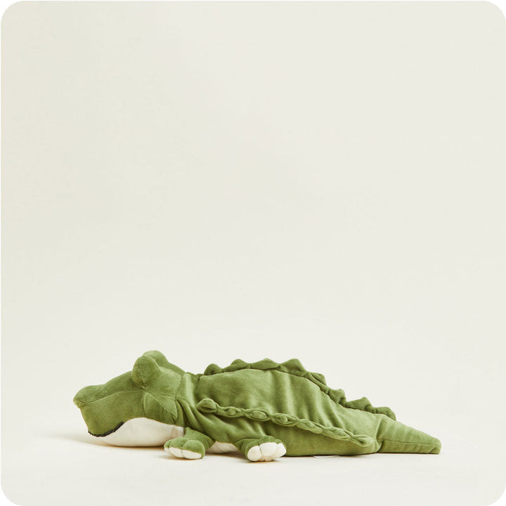 Green alligator Warmies plush heating pad with spikes and tail lying on white background