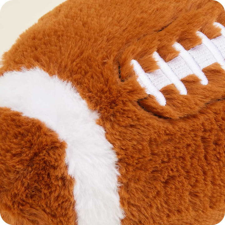 Warmies plush football-shaped heating pad in brown with white stitching details