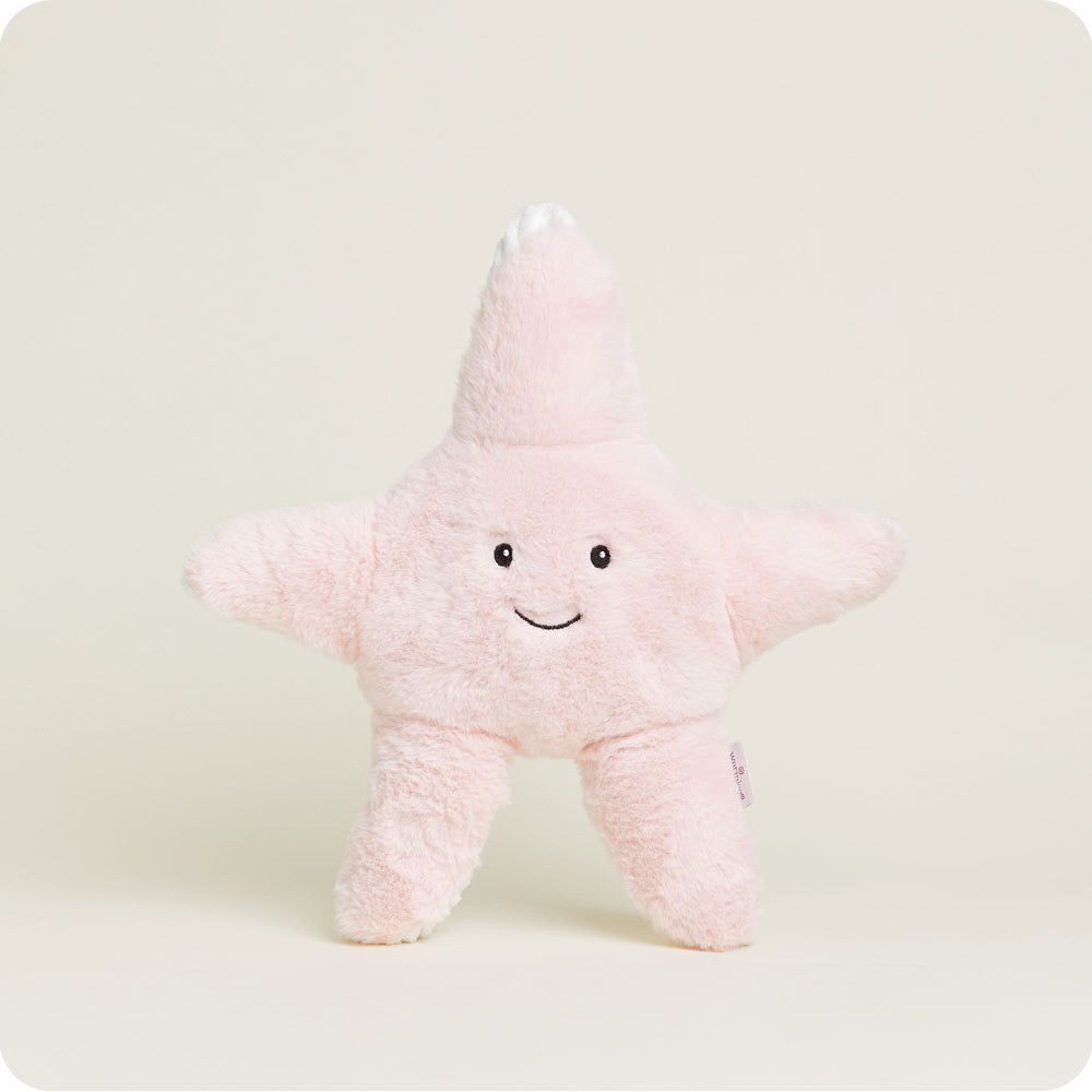 Pink fuzzy starfish-shaped Warmies plush toy with smiling face on white background