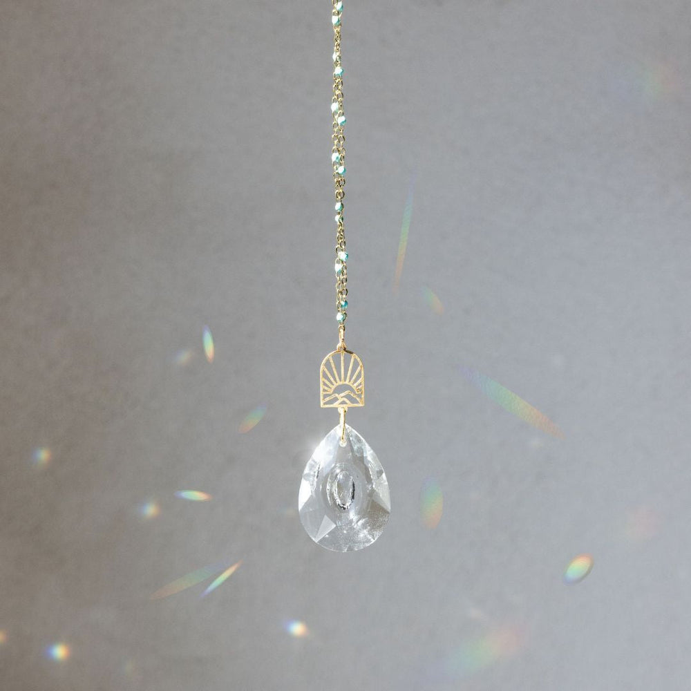 Scout Pocket Suncatcher with clear crystal teardrop and gold sunrise mountain charm creating rainbow light reflections