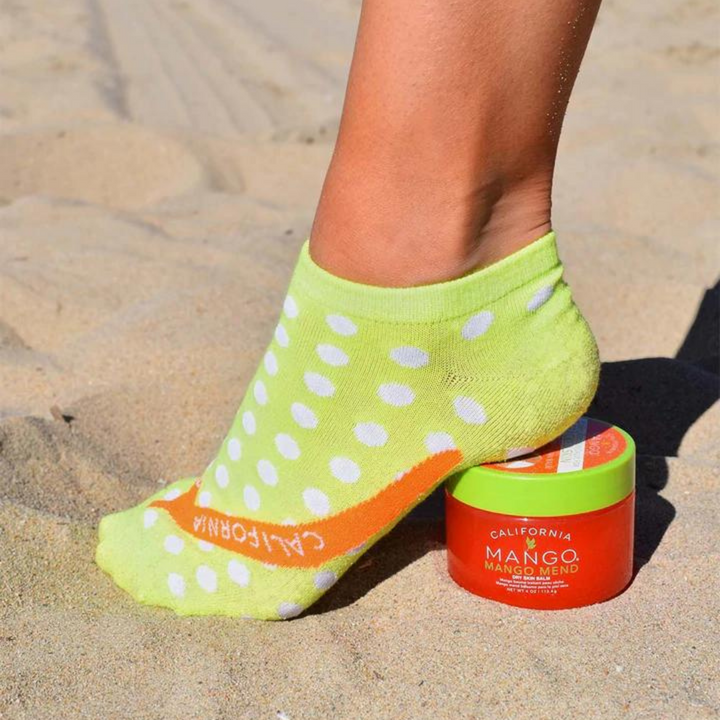 California Mango Dreaming Foot Spa Kit with lime green polka dot socks and Mango Mend balm on sand.
