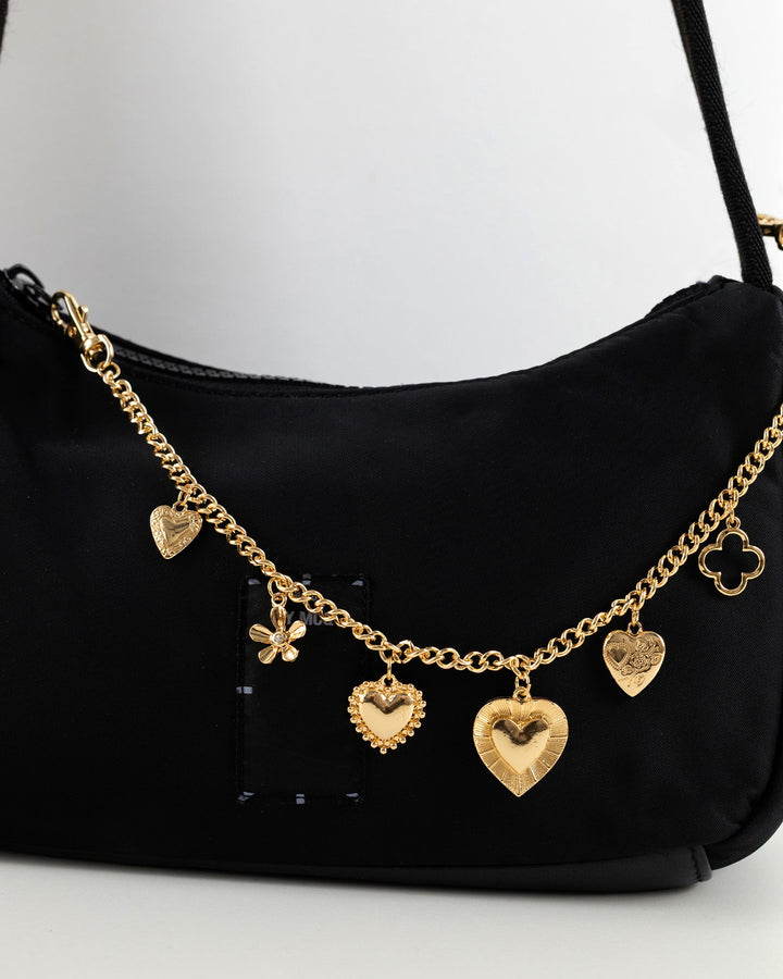 Gold heart and clover charm chain attached to a black shoulder bag by Sessori.