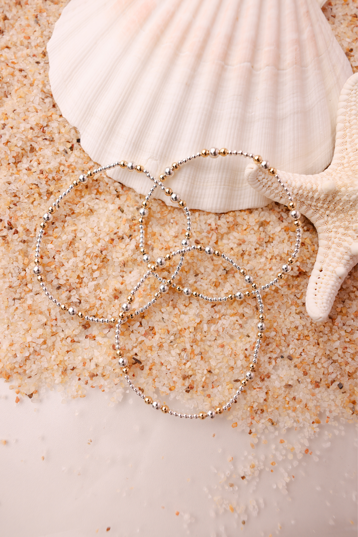 Dainty Beaded Blondes Sutton bracelets in silver with gold beads displayed on sand with seashell