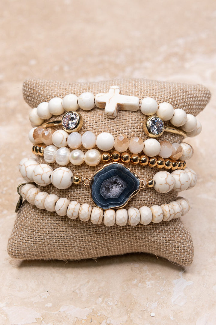 Six-piece white beaded bracelet stack with gold accents, cross charm, and blue geode centerpiece