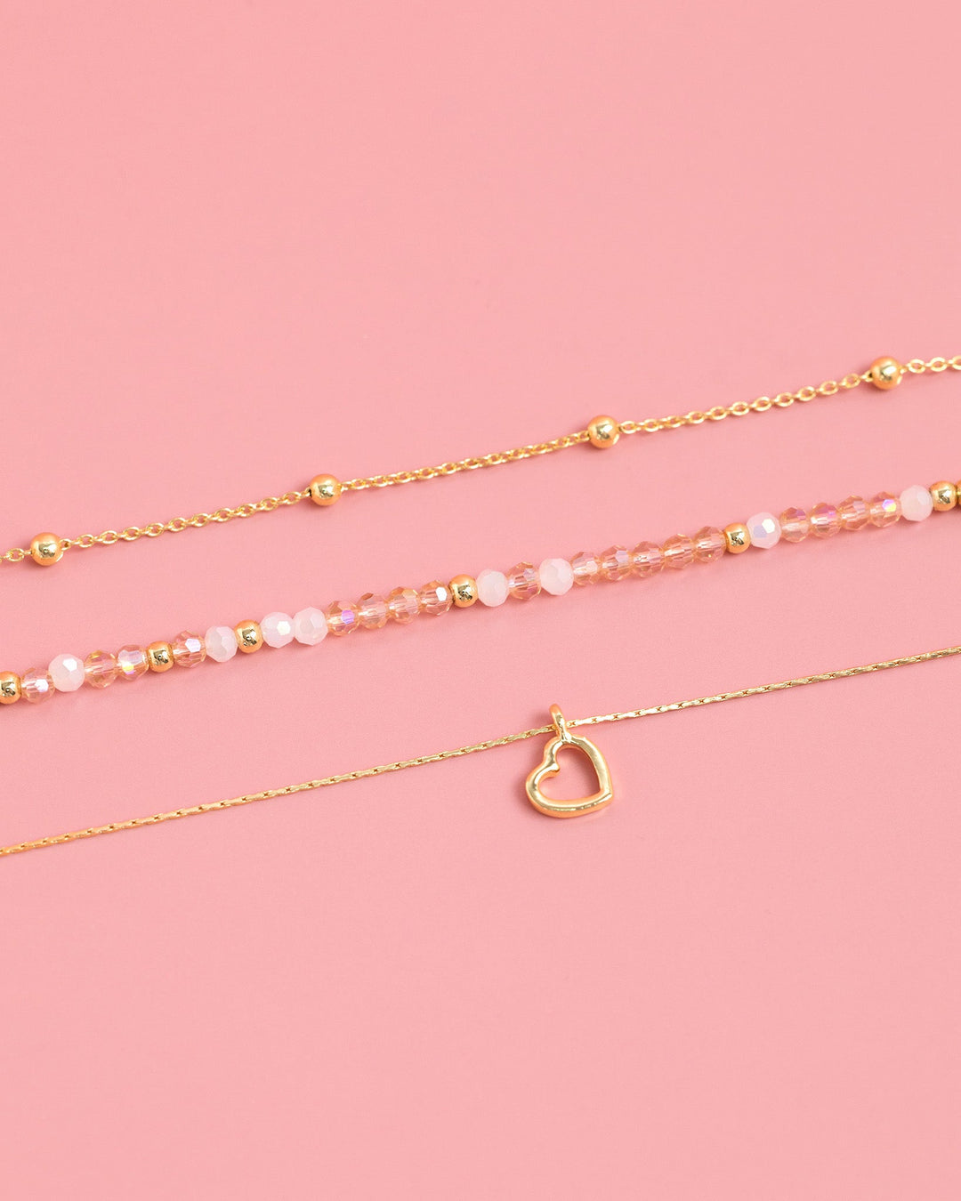 Set of three gold bracelets with blush pink beads and a delicate heart charm pendant