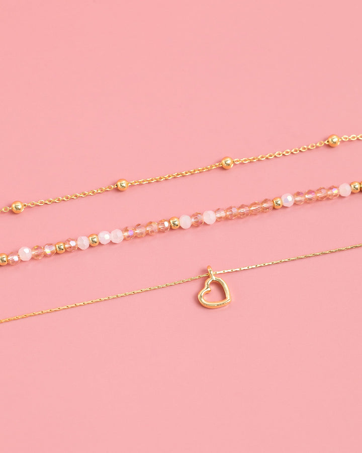 Set of three gold bracelets with blush pink beads and a delicate heart charm pendant