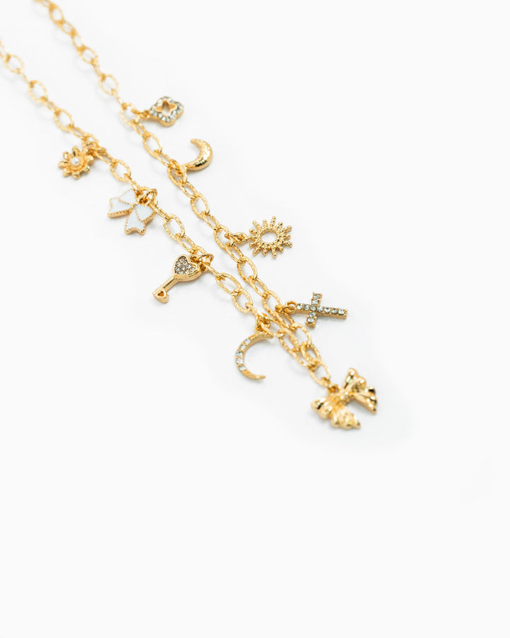 Gold multi-charm necklace featuring sun, moon, cross, butterfly, bow, and key charms with crystals