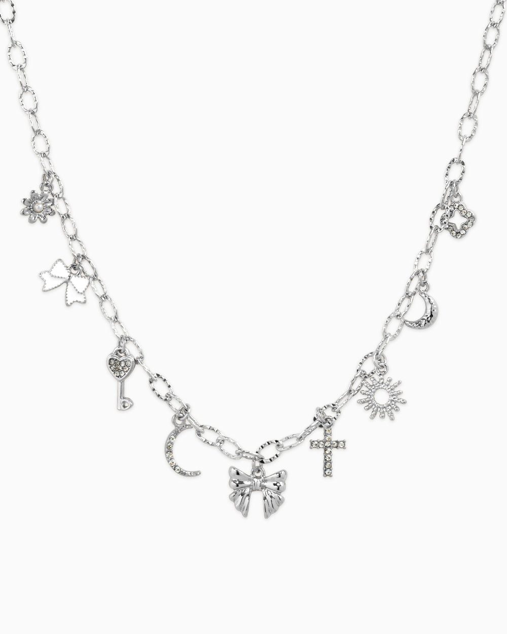 Silver charm necklace featuring bow, sunburst, cross, moon, key, and flower charms with crystal accents.