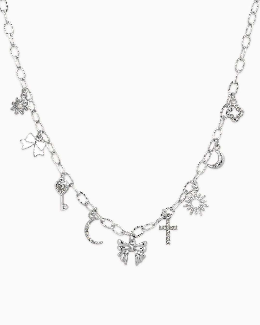 Silver charm necklace featuring bow, sunburst, cross, moon, key, and flower charms with crystal accents.