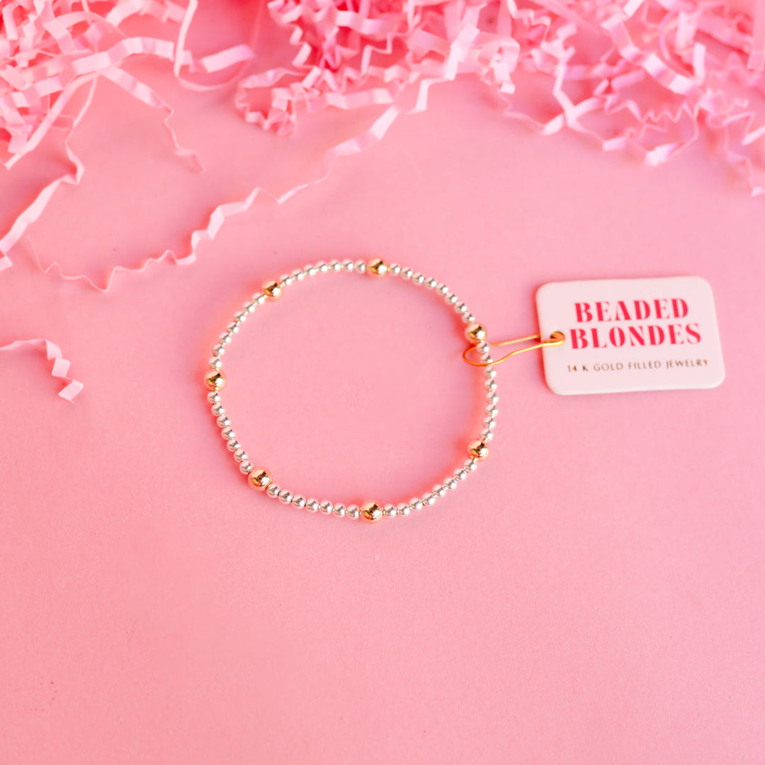 Beaded Blondes Olive Bracelet in silver with gold accent beads on pink background with brand tag.