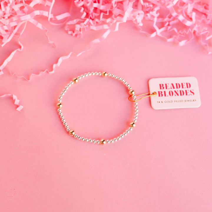 Beaded Blondes Olive Bracelet in silver with gold accent beads on pink background with brand tag.