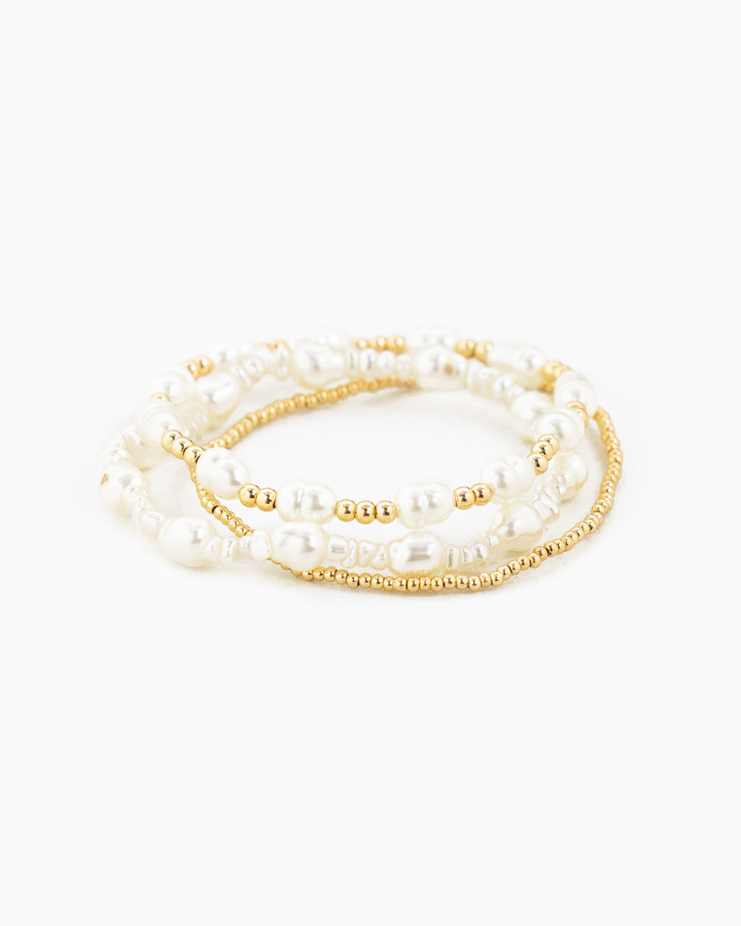 Set of three stretch bracelets featuring white pearls and gold beads stacked together