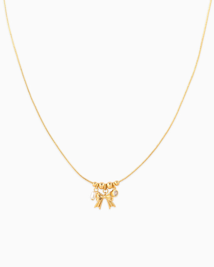 Dainty gold necklace with bow charm, small pearl, and crystal accent pendants