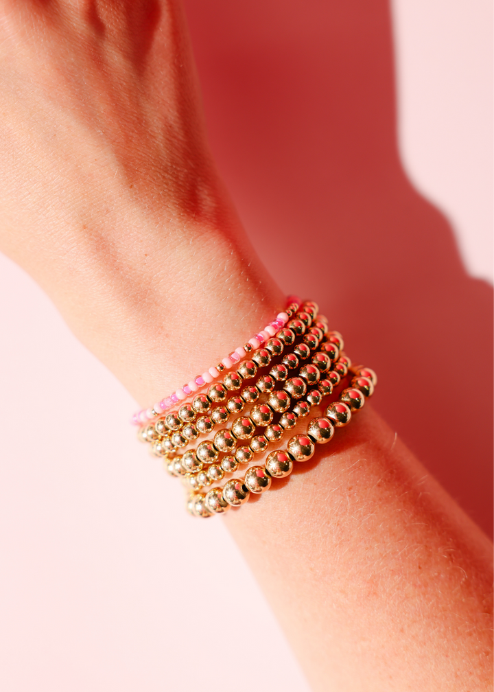 Stack of gold beaded bracelets with pink flamingo sprinkle accents worn on wrist