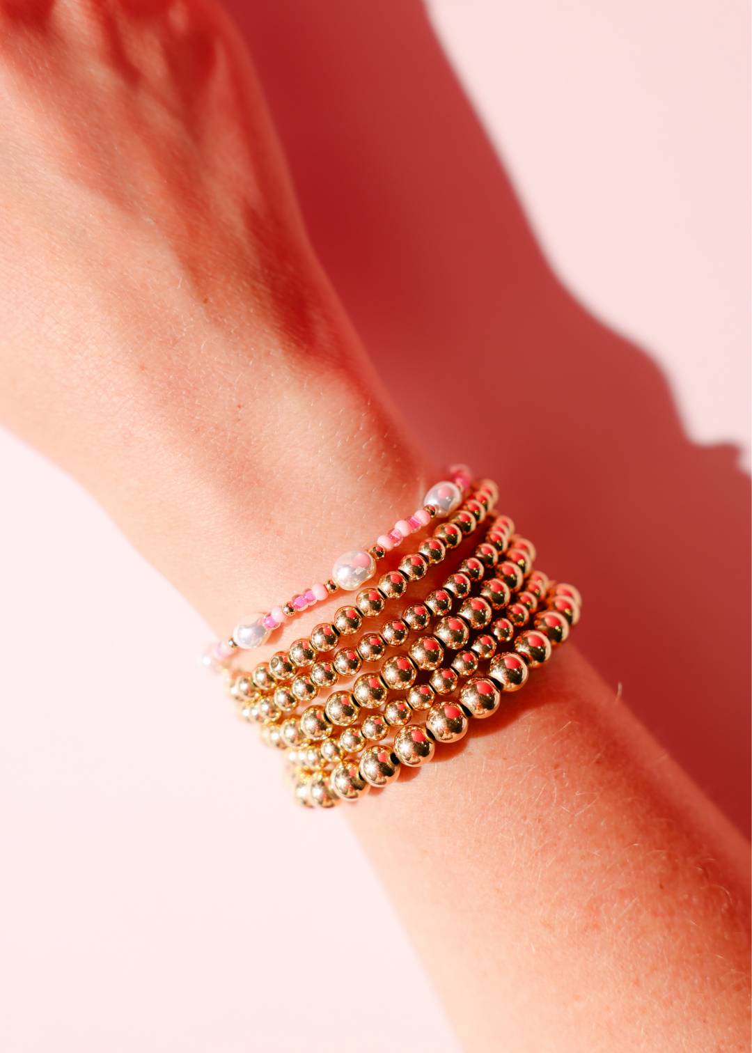 Stack of gold beaded bracelets with pink flamingo sprinkle accents worn on wrist.
