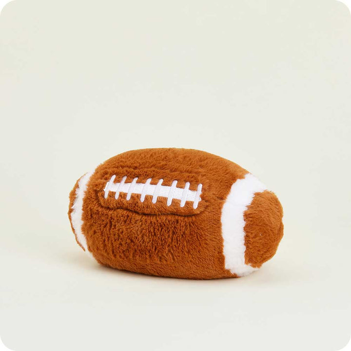 Warmies football-shaped plush toy with brown fabric and white laces against neutral background