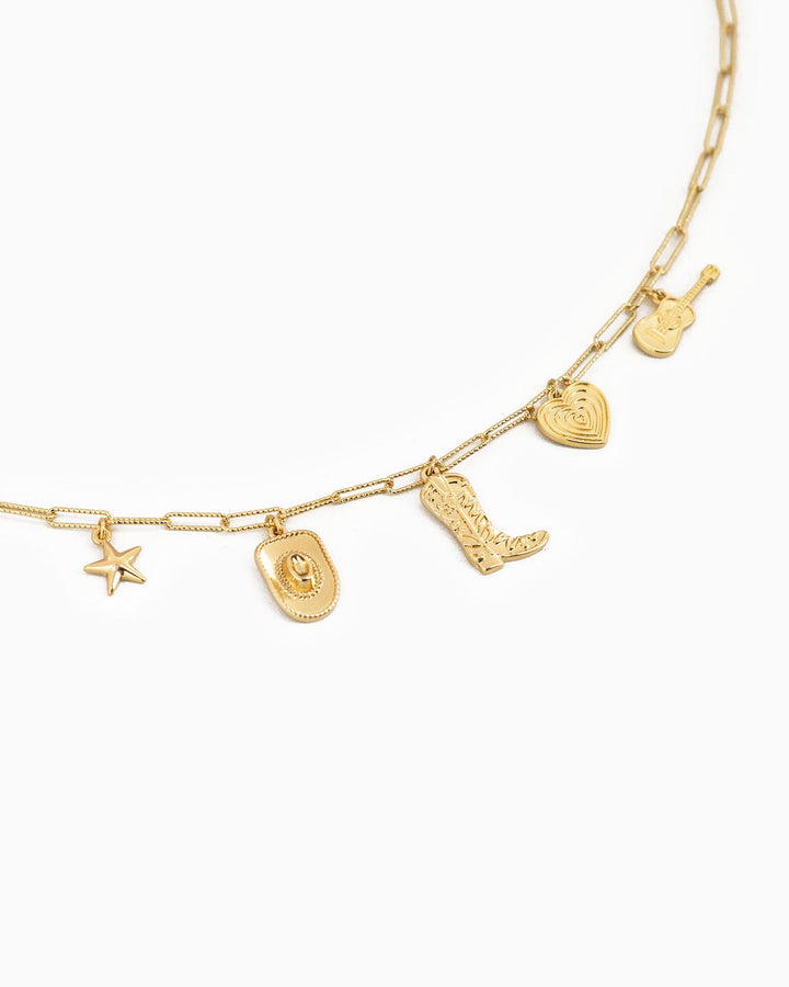 Gold charm necklace featuring western-themed charms including cowboy hat, boot, heart, guitar, and star