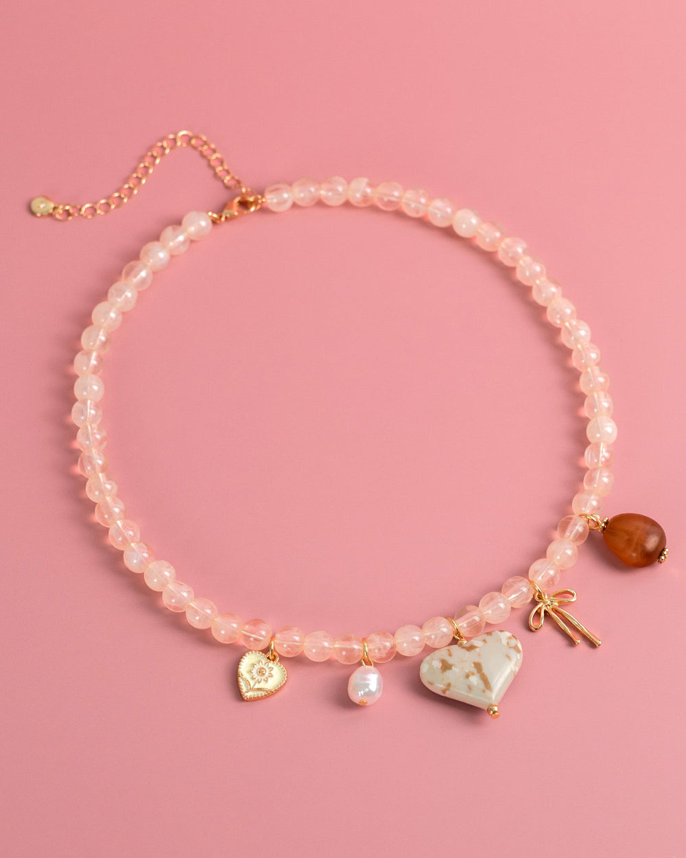 Pink beaded necklace with ivory marbled heart charm, pearl, bow, and amber pendant