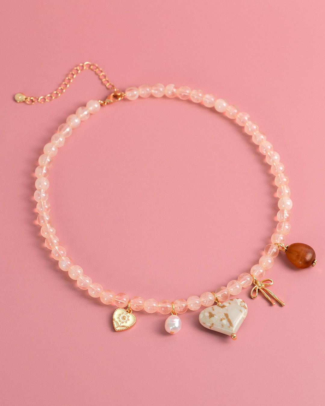 Pink beaded necklace with ivory marbled heart charm, pearl, bow, and amber pendant