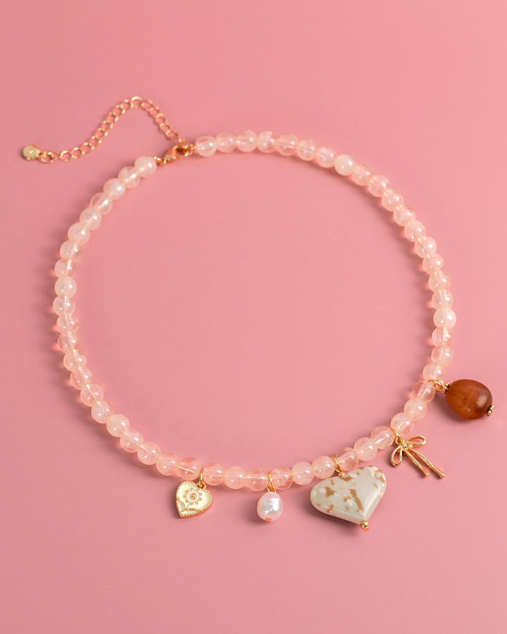 Pink beaded necklace with ivory marbled heart charm, pearl, bow, and amber pendant