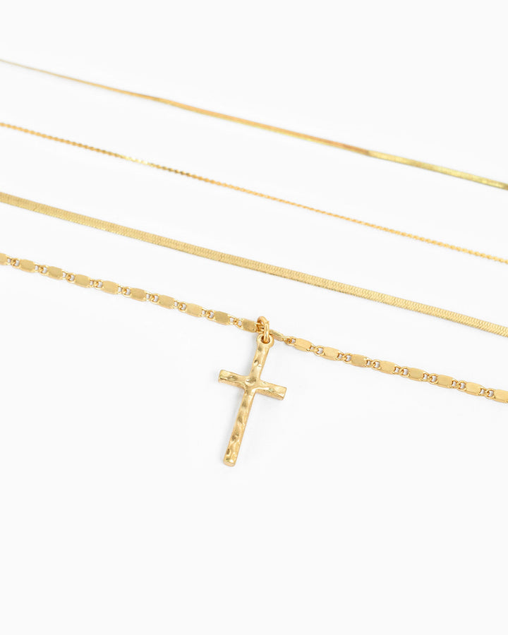Gold 4-layered snake chain necklace set with hammered cross pendant on white background.