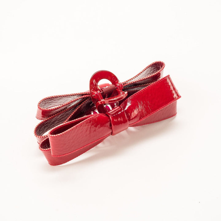 Red patent leather bow hair accessory with silver hardware on white background