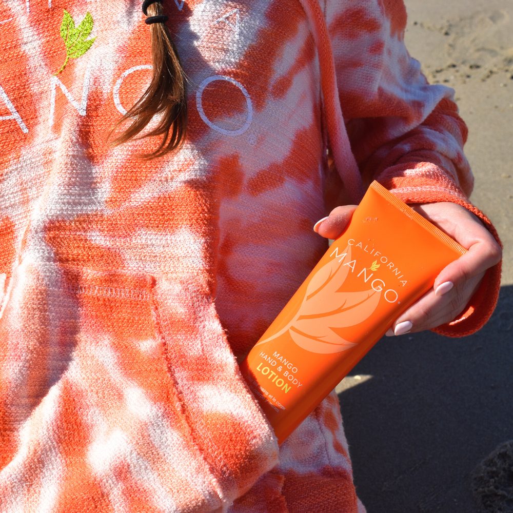 California Mango Hand and Body Lotion tube in vibrant orange held at the beach.