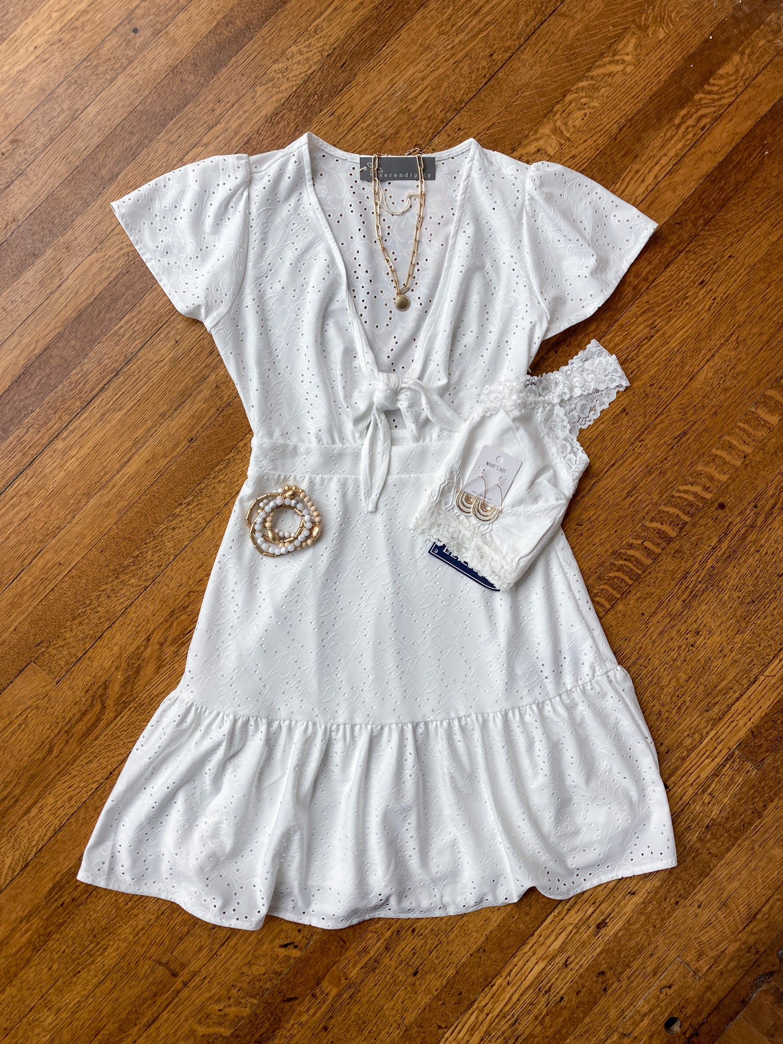 a flat lay image of a white summer dress with a gold necklace, gold bracelets and a white bralette.