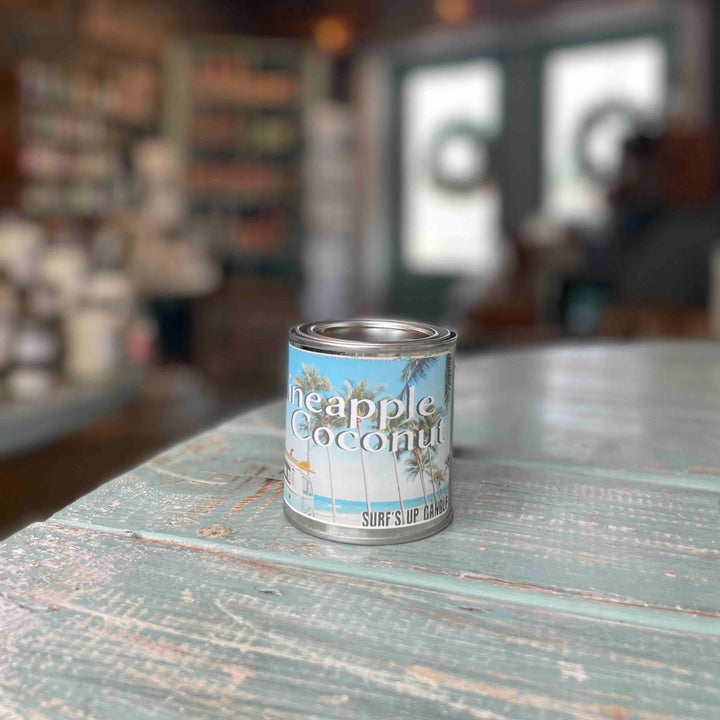 Surfs Up Candle Pineapple Coconut scented paint can candle pint sitting on a rustic teal wooden surface