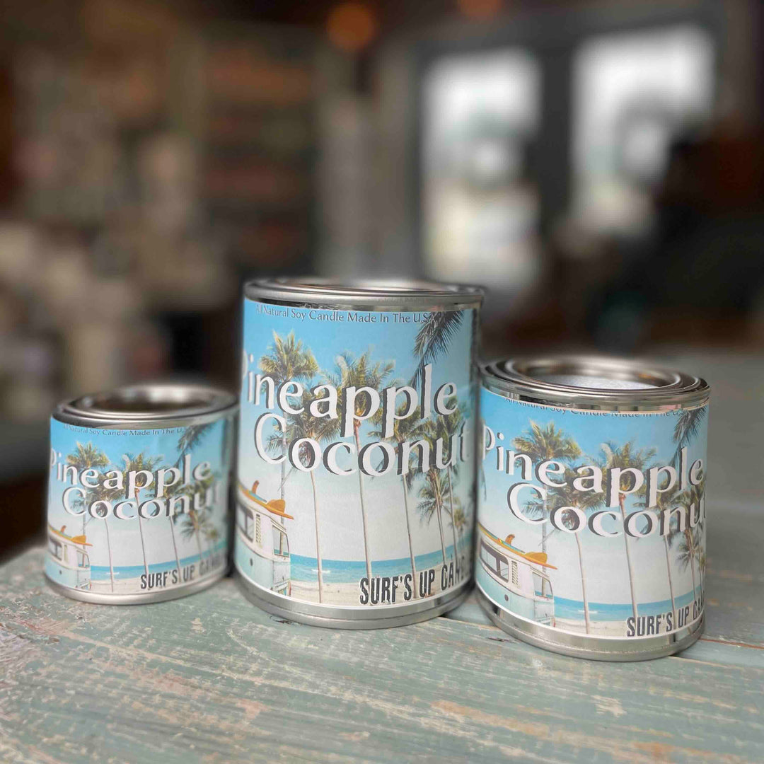 Surfs Up Candle Pineapple Coconut paint can candles in three sizes on a rustic surface