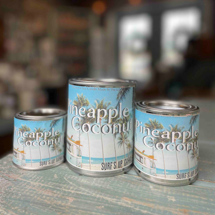 Surfs Up Candle Pineapple Coconut paint can candles in three sizes on a rustic surface