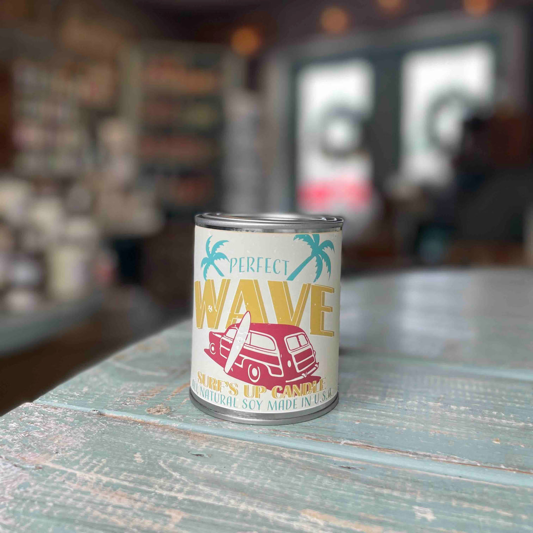 Surfs Up Candle Perfect Wave paint can pint candle with retro surf-themed label on weathered teal table.