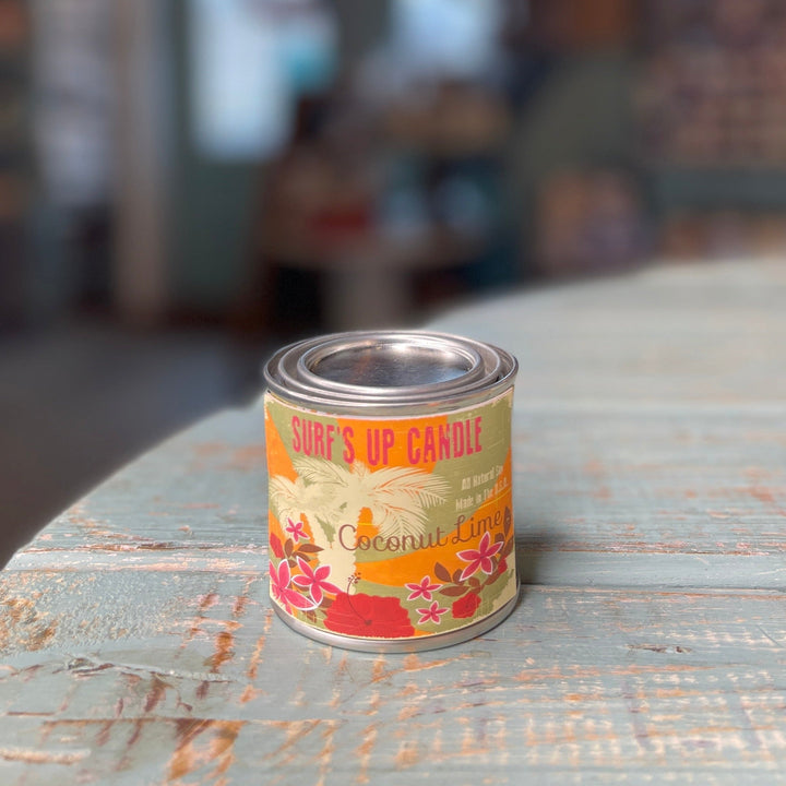Surf's Up Candle Coconut Lime scented paint can candle with tropical floral label on rustic table.
