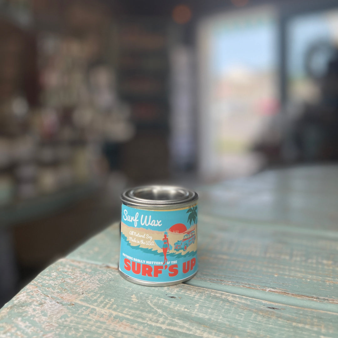 Surf Wax Paint Can Candle Pint in a small silver tin with retro beach-themed label on a weathered teal surface.