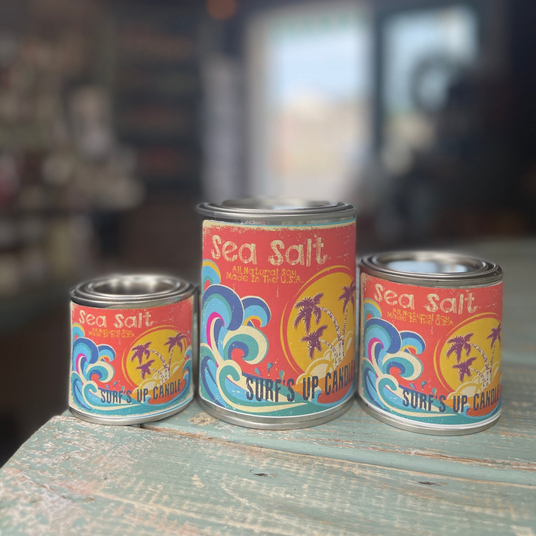 Surf's Up Candle Sea Salt paint can candles in three sizes on a rustic teal surface