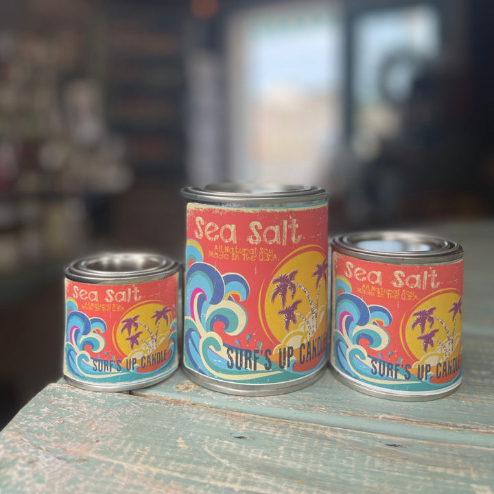 Surf's Up Candle Sea Salt paint can candles in three sizes on a rustic teal surface