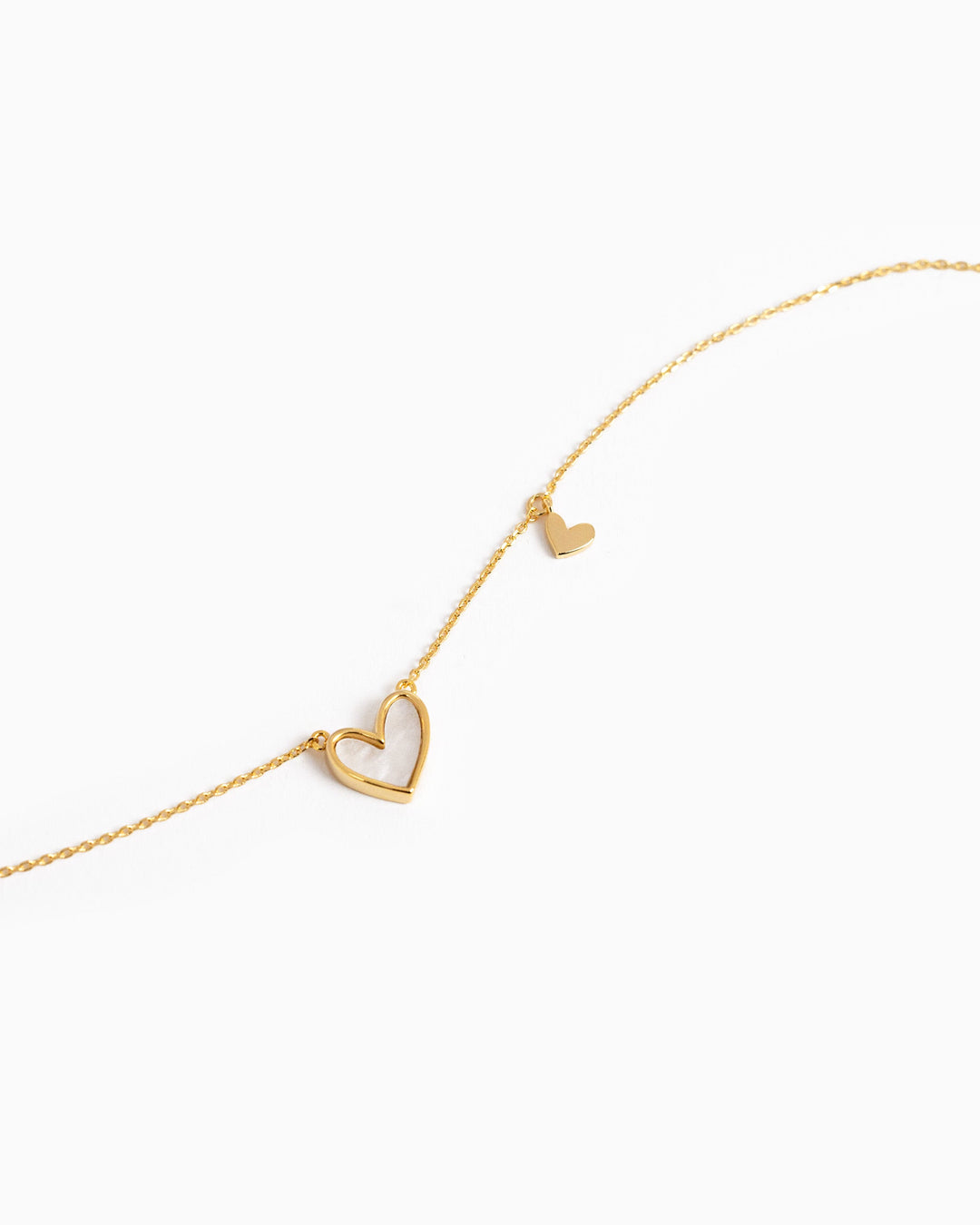Gold asymmetrical necklace featuring a large mother-of-pearl heart pendant and small solid gold heart charm