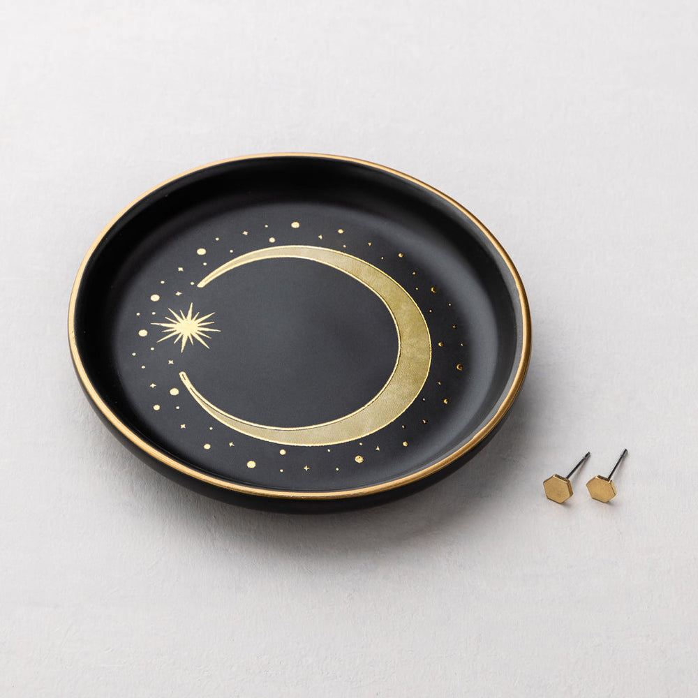 Black ceramic jewelry dish with gold crescent moon design and two small gold hexagon stud earrings