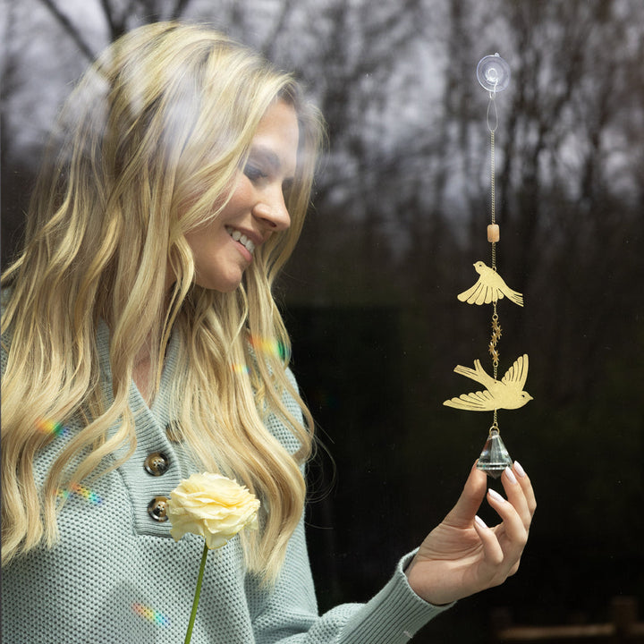 Scout gold bird suncatcher with crystal prism held by smiling blonde woman outdoors