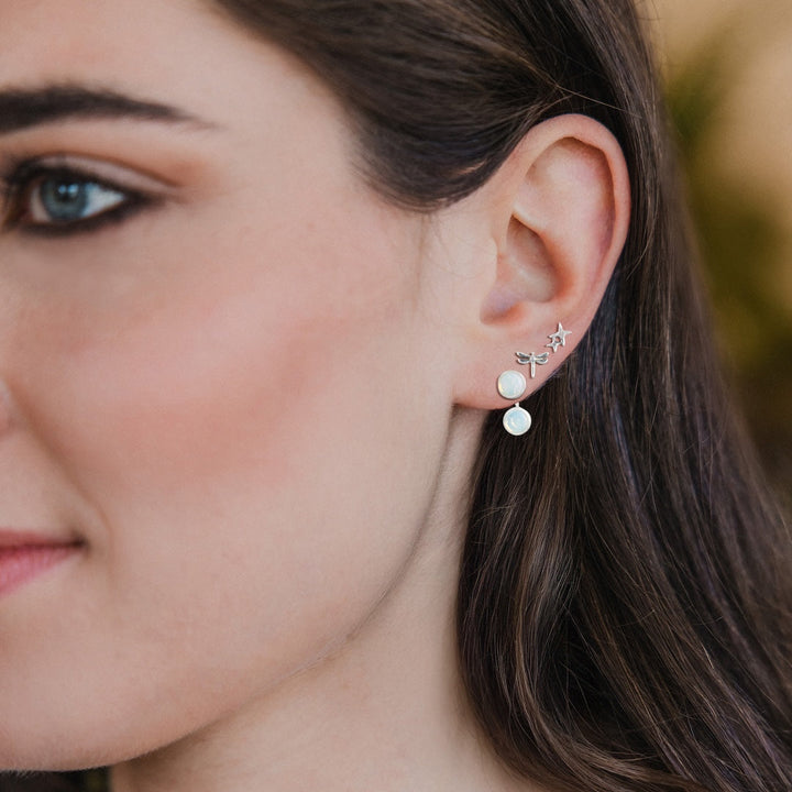 Woman wearing Scout Stud Trio Jacket Set earrings with silver star and dragonfly studs and white opal drops