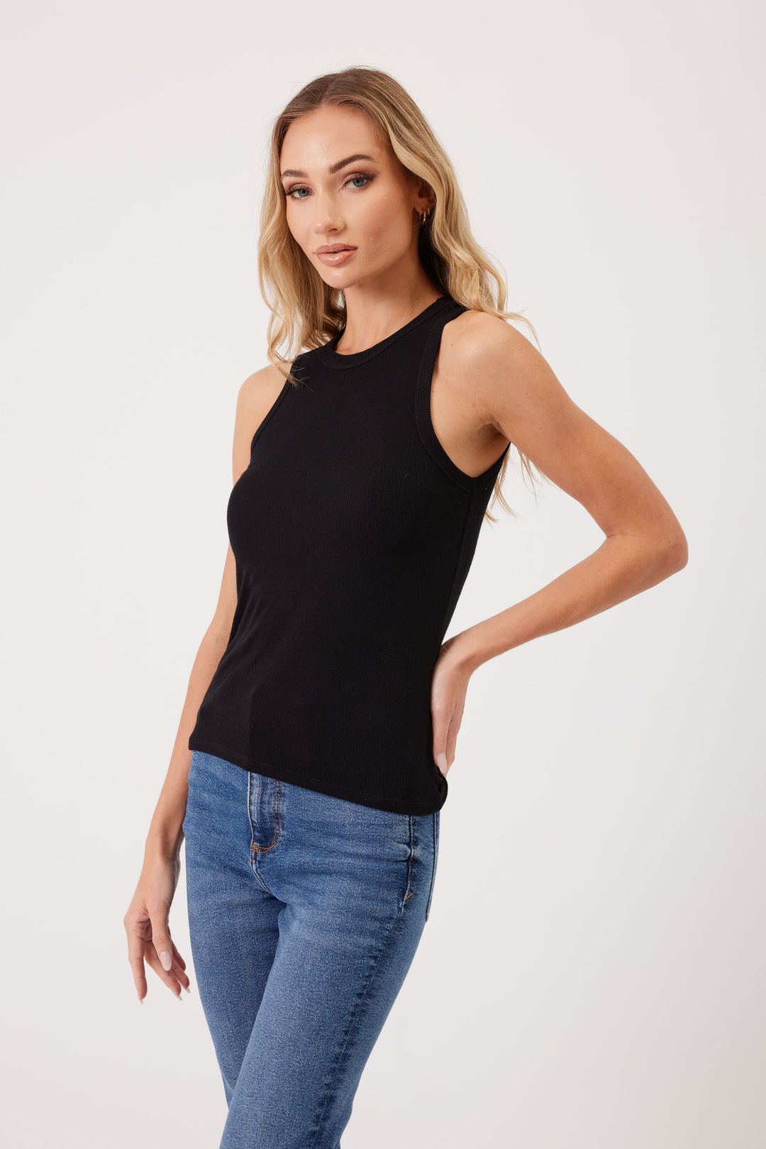 Woman wearing black sleeveless ribbed tank top with blue jeans on white background