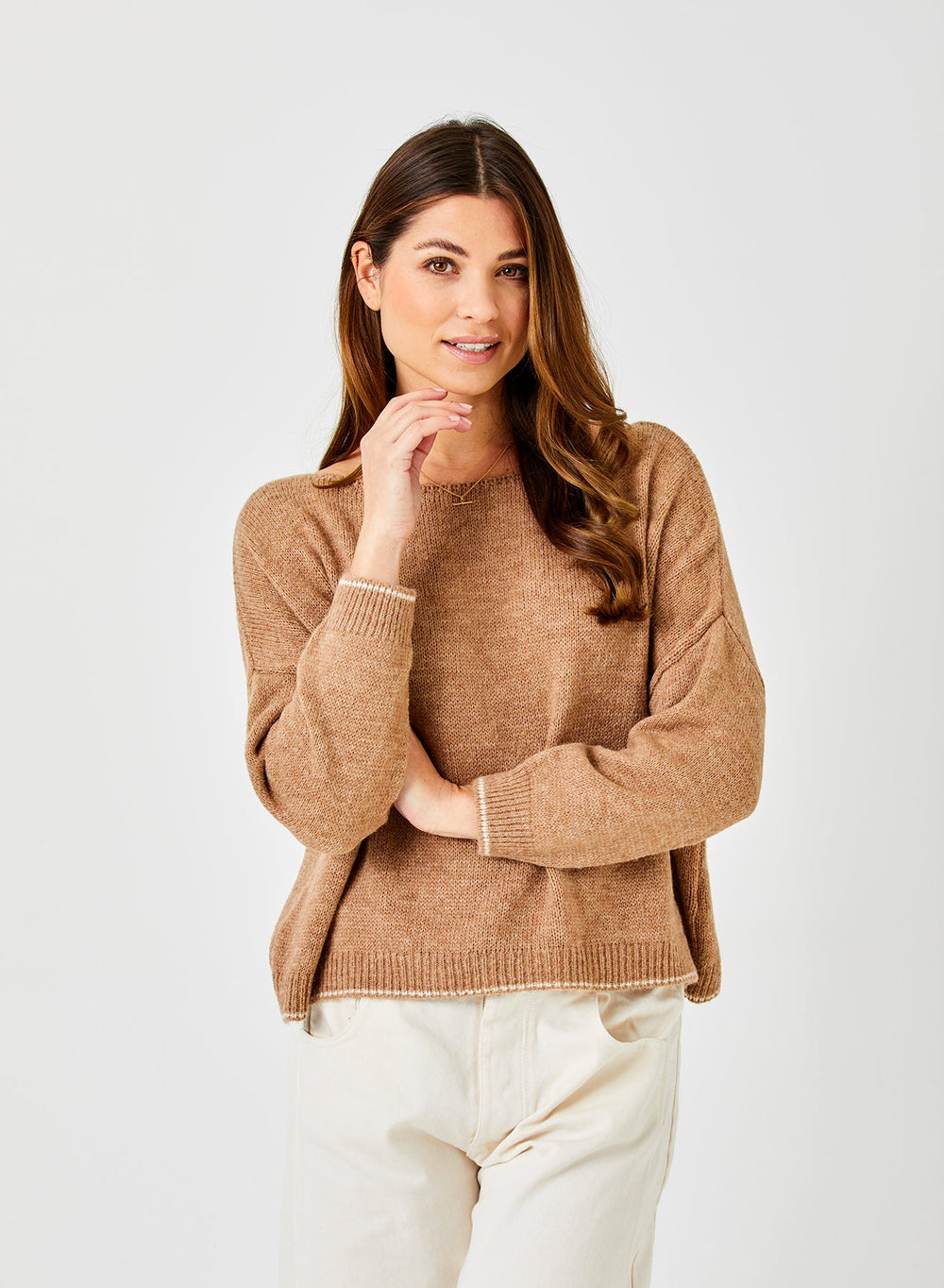 Woman wearing camel colored oversized knit sweater with cream pants against white background